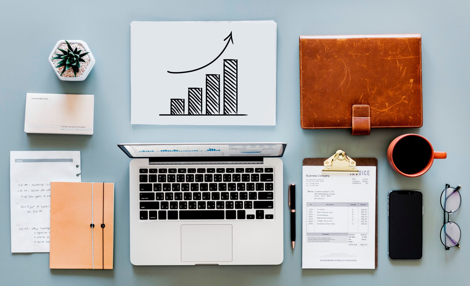 Image of a bookkeepers desk, with laptop, notebook, and graphs