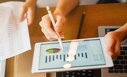 Hands using a tablet and laptop to analyze business reports and data visualizations.