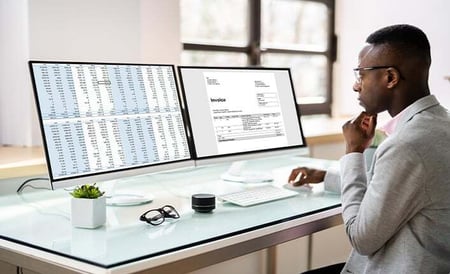 Person working at a desk with two computer screens displaying financial data, representing reliable subsidy tracking through agency ledgers.