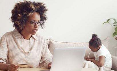Woman working on a laptop with a child nearby, illustrating flexible billing management.