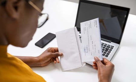 Person reviewing documents and using a laptop, symbolizing accurate and reliable administrative processes for getting paid on time.