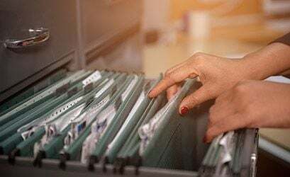 Hands opening a file drawer with many folders, symbolizing comprehensive record keeping.