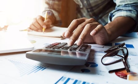 Hands using a calculator and writing notes on paper, representing transparent financial planning.