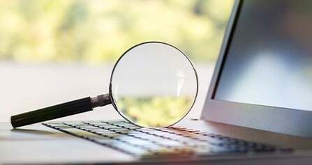 A magnifying glass resting on a laptop keyboard, indicating detailed financial analysis or reporting.