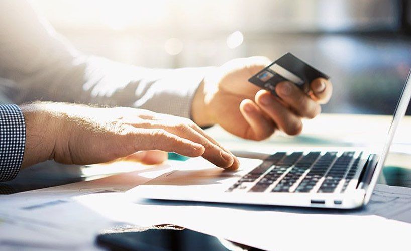 Person holding a credit card while typing on a laptop, indicating online payments or financial management.