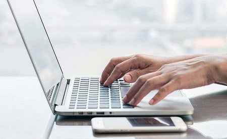 Hands typing on a laptop with a smartphone nearby, symbolizing efficient digital solutions.