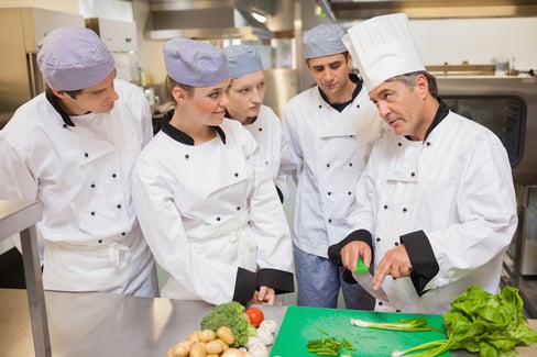 Trainees learning vegetable slicing in the kitchen
