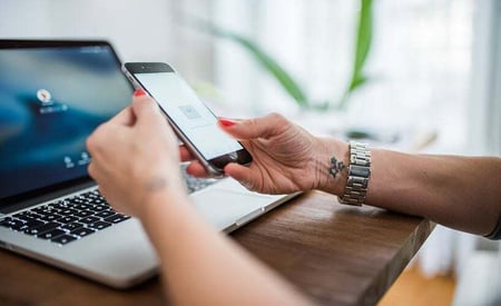 Person making a seamless payment within an app on a smartphone, with a laptop in the background, representing integrated billing and payment.